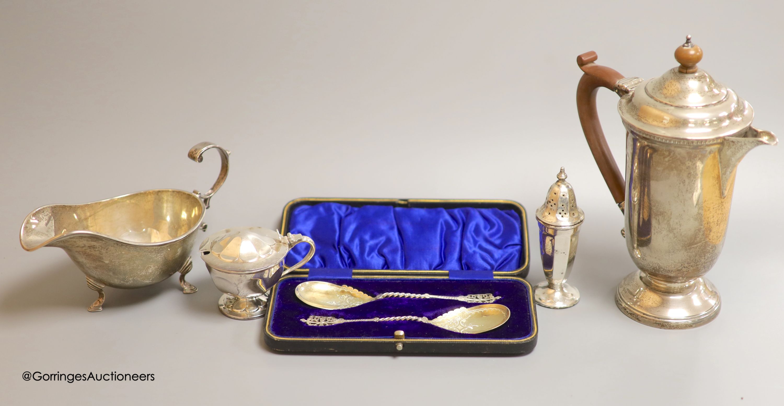 A cased pair of ornate Edwardian silver preserve spoons, Sheffield, 1905, a silver sauceboat, a silver hot water pot and two silver condiments